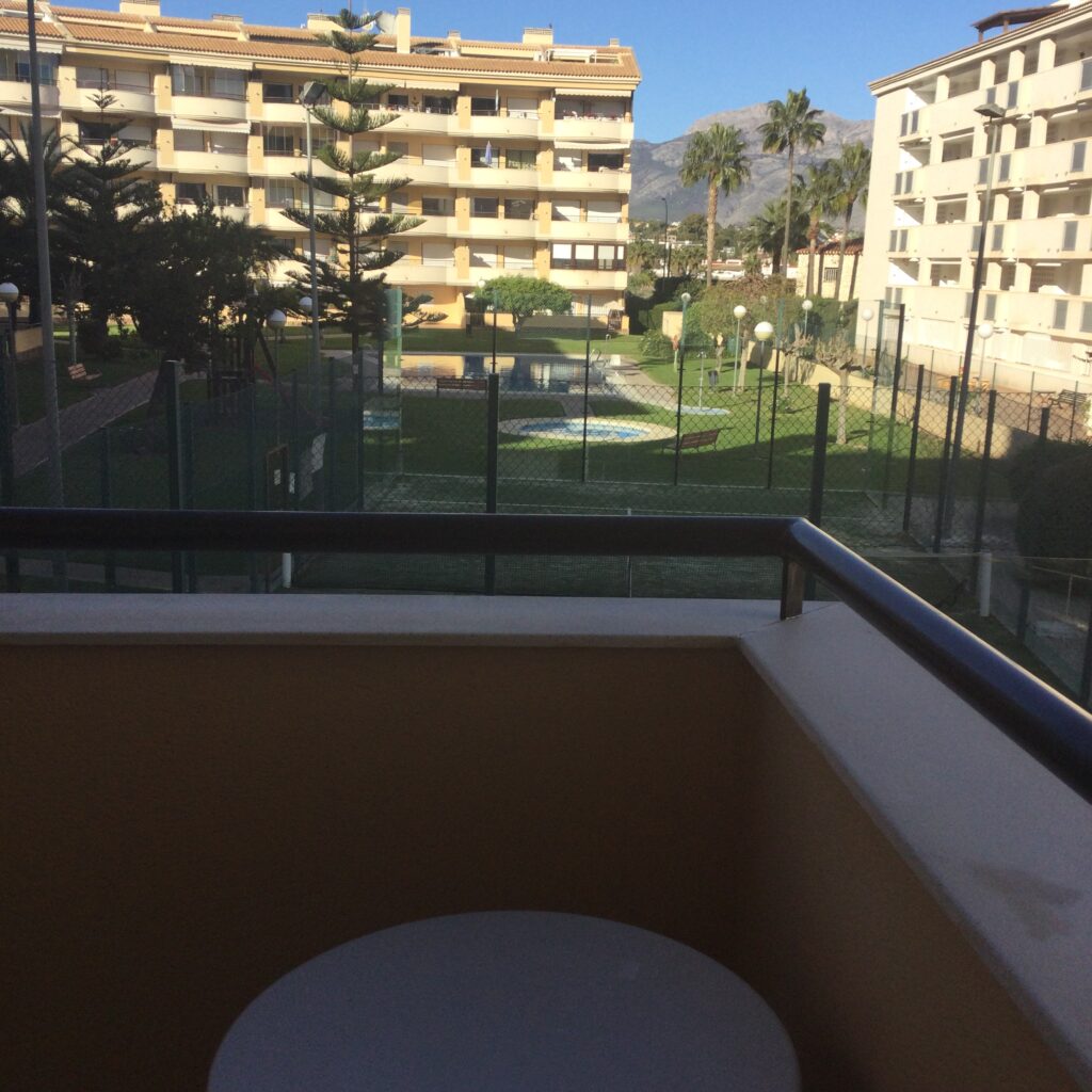een hoekje van het balkon en uitzicht op padelbaan en zwembad